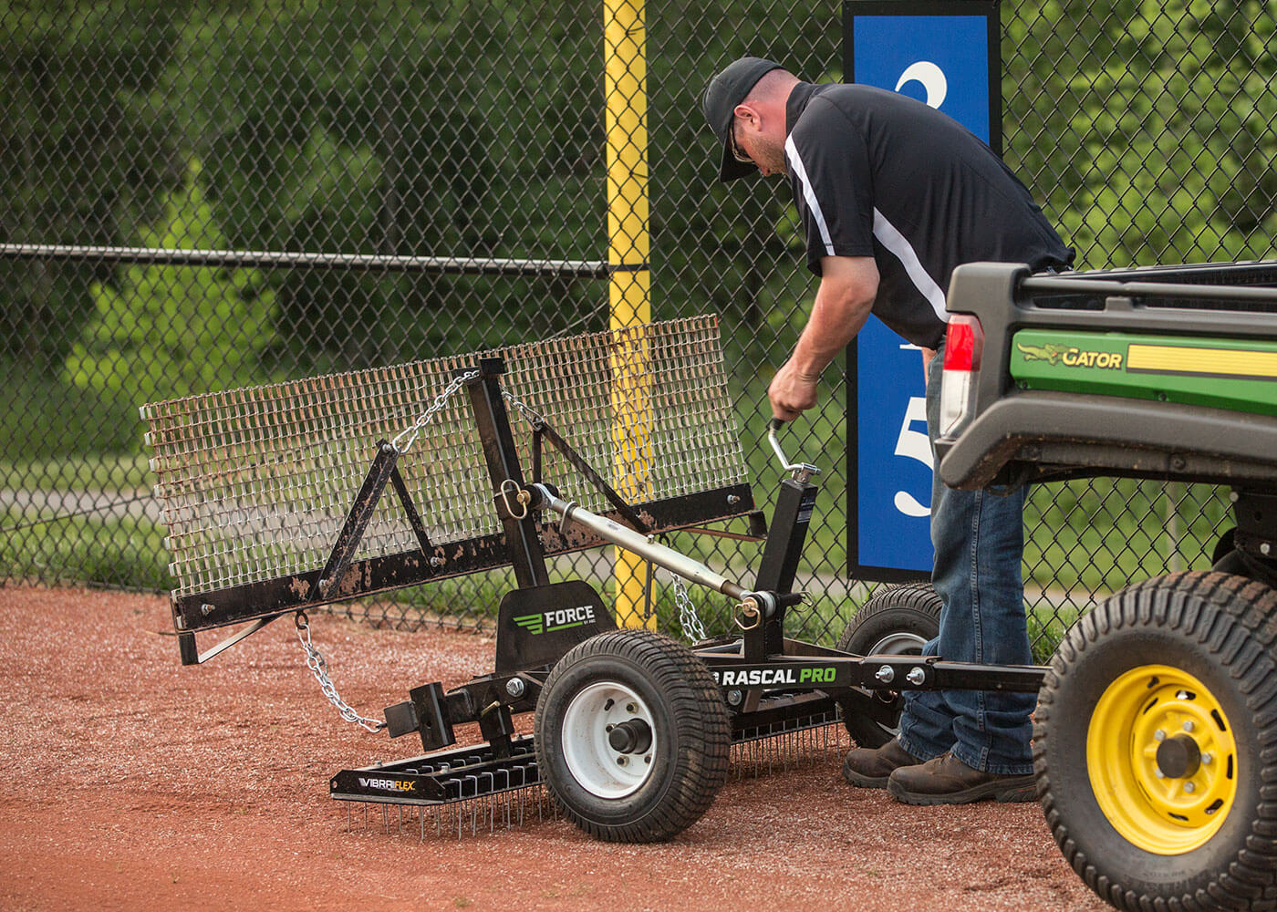 Man adjusting attachment on infield rascal pro pull-behind groomer with vibraflex and rigid drag mat attachment
